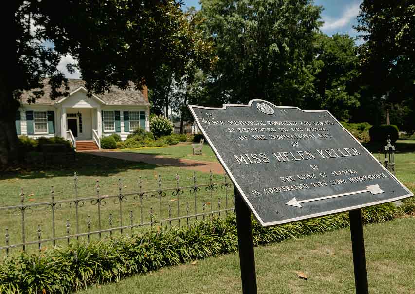 white house with green shutters and large trees on lawn